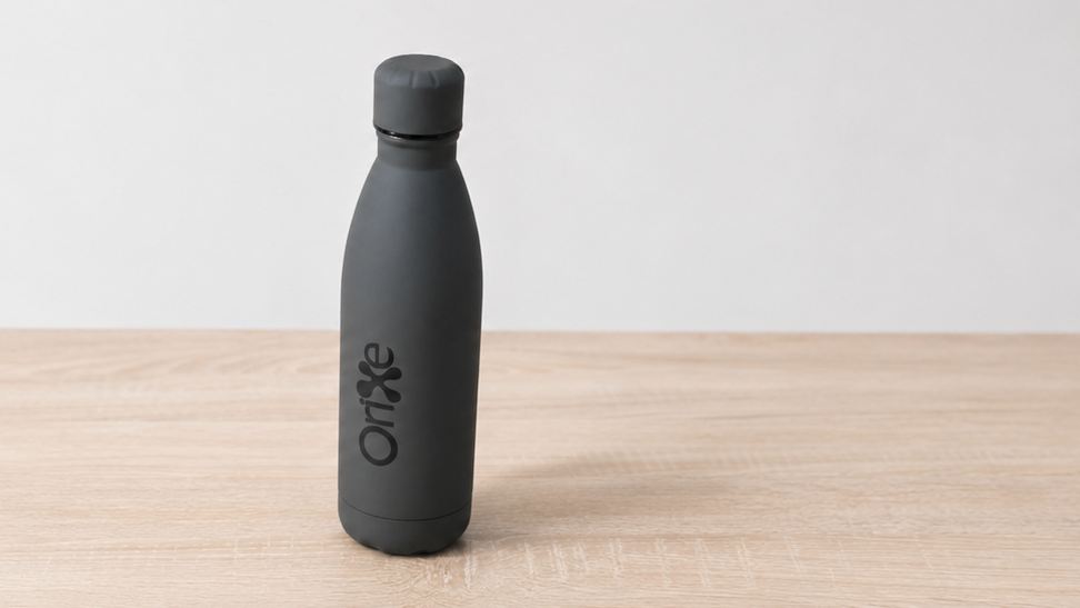 Botella corporativa gris de Orixe Publicidade con logotipo negro sobre mesa de madera