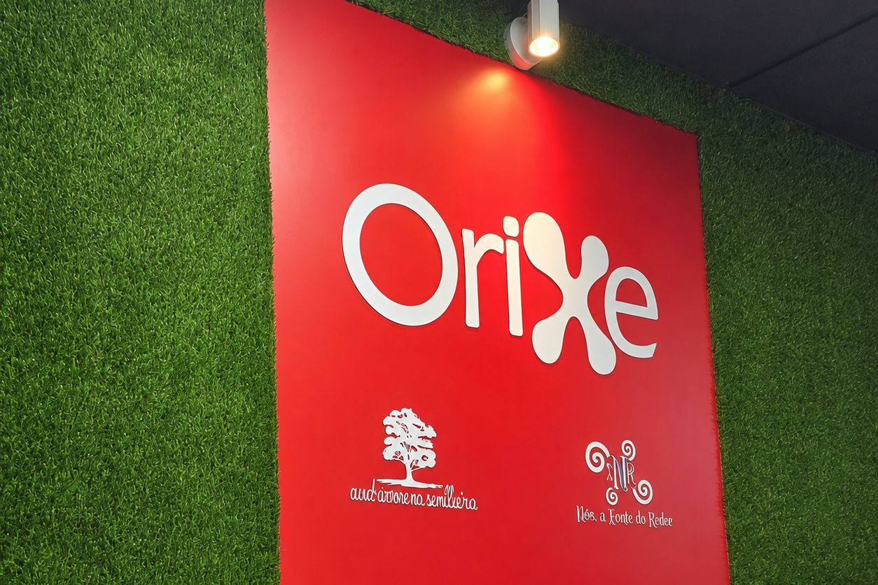 Nueva imagen corporativa de Orixe Publicidade con logotipo en PVC sobre panel rojo y césped artificial
