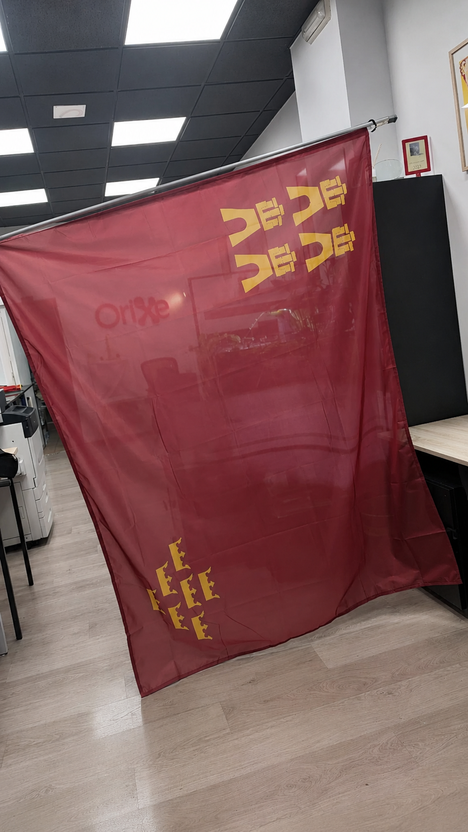 Bandera textil personalizada murcia Bandera textil burdeos semitransparente con símbolos dorados, fotografiada en interior de taller.