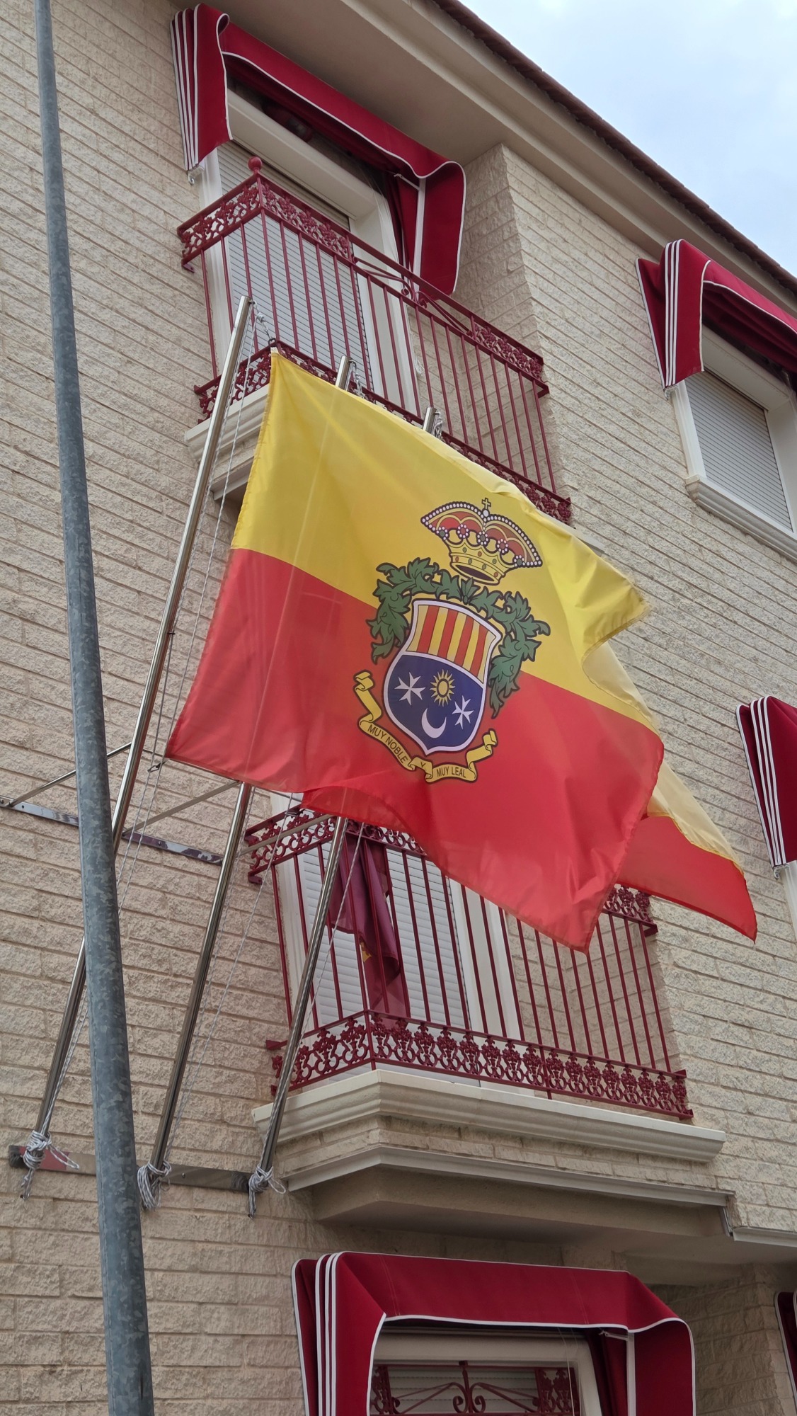 Bandera exterior personalizada con escudo Bandera exterior roja y amarilla con escudo, instalada en fachada mediante soporte metálico. bandera archena